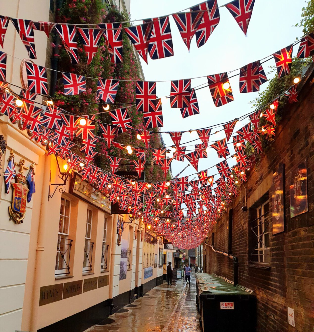 Narrow alley decorated with abundant Union Jack bunting and string lights, creating a vibrant British atmosphere.