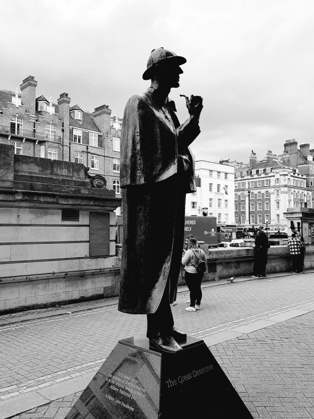 Statue of Sherlock Holmes, 'The Great Detective', in London. The black and white image shows the iconic figure with a pipe against a backdrop of classic British architecture.