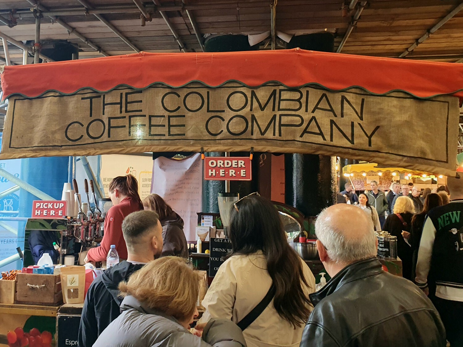 The Colombian Coffee Company stall at a bustling market, with customers waiting to order.