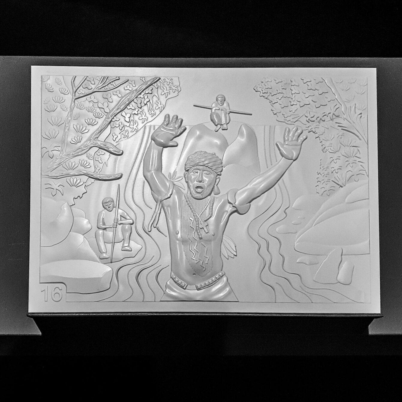 A monochrome sculptural relief panel, numbered 16, showing a central indigenous figure with arms raised wide, standing waist-deep in a stylised river. Two smaller figures with spears are visible in the background, surrounded by trees and flowing water. Part of the Amazônia exhibition by Sebastião Salgado at the Rautenstrauch-Joest Museum, Cologne.